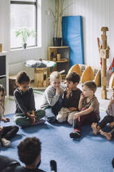 Multirassische Jungen und Mädchen mit Fingern auf den Lippen sitzen im Kindergarten - MASF34553