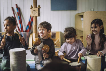 Multiracial male and female students enjoying while playing drum kit in kindergarten - MASF34555