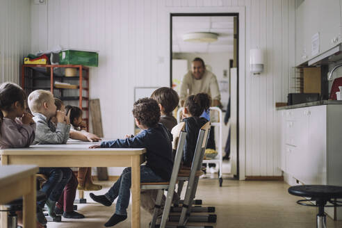 Männliche und weibliche Schüler verschiedener Rassen sitzen beim Frühstück im Kindergarten am Esstisch - MASF34566