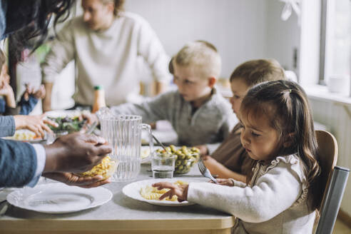 Teacher serving food to male and female students for breakfast in day care center - MASF34572