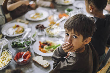 Porträt eines Jungen, der den Mund mit der Hand bedeckt, während das Frühstück auf dem Tisch einer Kindertagesstätte steht - MASF34582