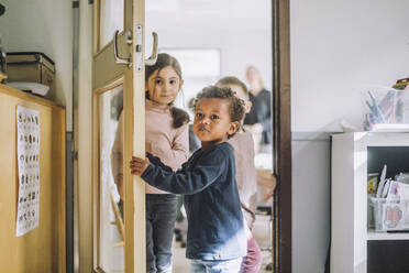 Junge, der die Tür öffnet, während er mit seinen Klassenkameraden vor der Tür des Kindergartens steht - MASF34592