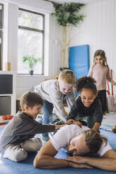 Cheerful multiracial children playing with male teacher in day care center - MASF34608