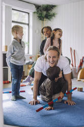 Happy male teacher enjoying with male and female students in day care center - MASF34610