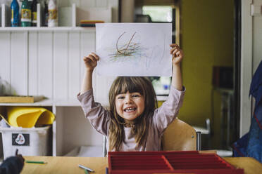 Portrait of happy girl showing color pencil scribble on paper at kindergarten - MASF34622