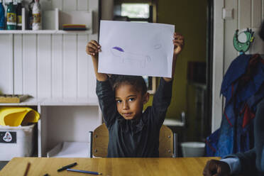 Portrait of student showing drawing on paper in day care center - MASF34625