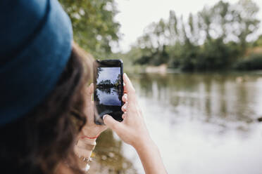 Frau, die am See im Park Fotos mit ihrem Smartphone macht - MRRF02569