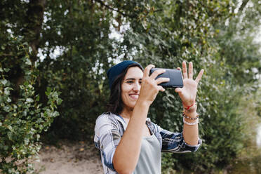 Lächelnde junge Frau, die mit ihrem Smartphone im Park Fotos macht - MRRF02570