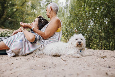 Freunde sitzen im Sand bei einem Hund im Park - MRRF02579