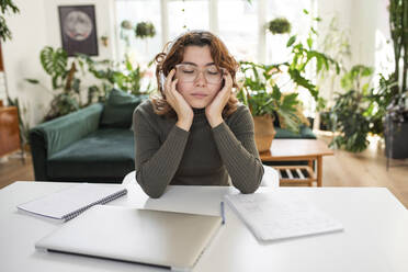 Freelancer with eyes closed sitting on table at home - VRAF00026