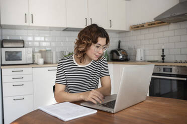 Freelancer using laptop on table in kitchen at home - VRAF00058