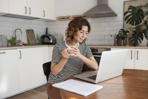 Freiberufler mit Kaffeetasse und Laptop auf dem Tisch zu Hause - VRAF00059