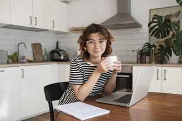 Freelancer with cup of coffee sitting with laptop at table - VRAF00060