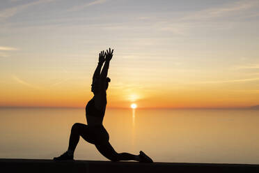 Frau mit erhobenen Armen übt Yoga vor dem Meer - LJF02458