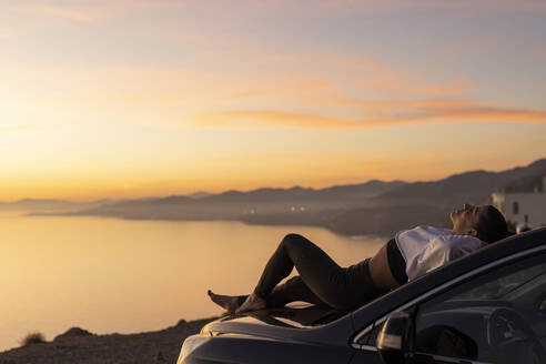 Woman relaxing on hood of car at sunset - LJF02461