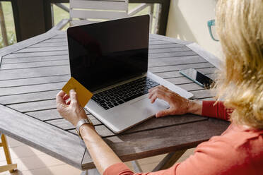 Frau mit Kreditkarte beim Online-Shopping mit Laptop am Tisch - MMPF00582