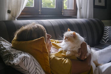 Senior woman cuddling with cat on sofa at home - MMPF00586