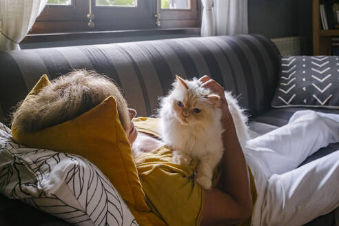 Ältere Frau mit Katze kuschelnd auf dem Sofa zu Hause - MMPF00587