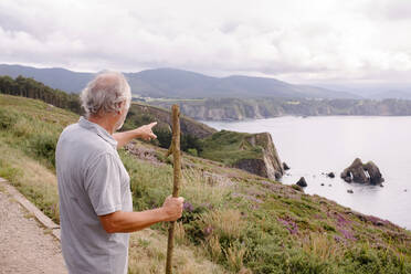 Älterer Mann mit Stock, der auf Berge zeigt - MMPF00611