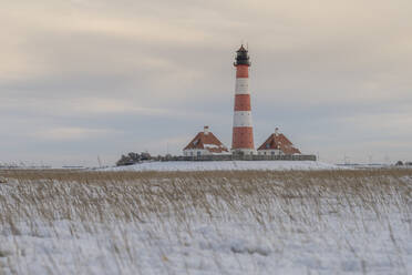 Germany, Schleswig-Holstein, Westerhever, Snow-covered field in front of Westerheversand Lighthouse - KEBF02560