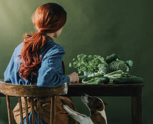 Rothaarige Frau sitzt auf einem Stuhl mit grünem Gemüse - VSNF00354