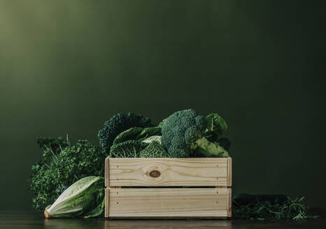 Crate full of fresh raw vegetables in front of green wall - VSNF00362