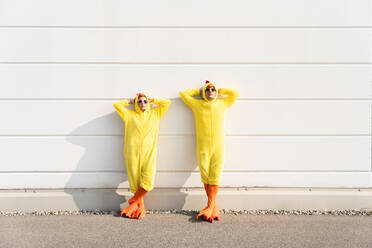 Woman and man wearing chicken costumes leaning with hands behind head on wall - OIPF02867