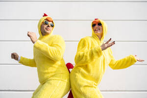 Glückliche Frau und Mann in gelben Hühnerkostümen haben Spaß vor einer Wand - OIPF02880