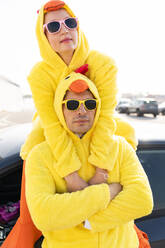 Freunde mit Sonnenbrillen und gelben Hühnerkostümen vor einem Auto - OIPF02903