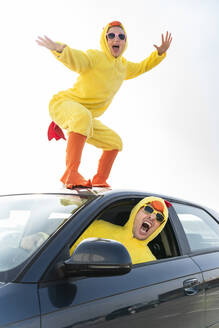 Mann fährt Auto mit unbekümmerter Frau im Hühnerkostüm, die auf dem Dach tanzt - OIPF02904