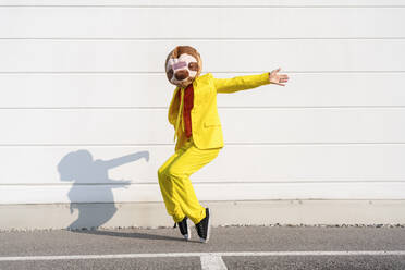 Playful man wearing animal mask dancing in front of wall - OIPF02912