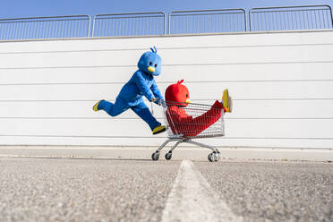 Mann und Frau in Entenkostümen spielen mit Einkaufswagen an der Wand - OIPF02963