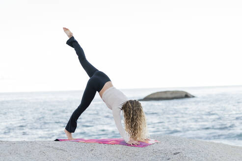 Frau übt Yoga auf einem Felsen vor dem Meer - MEF00154