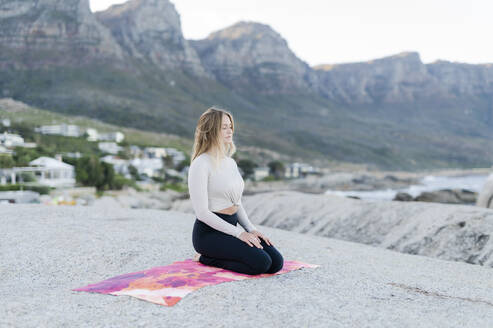 Junge Frau meditiert auf einem Felsen mit Bergkette im Hintergrund - MEF00156