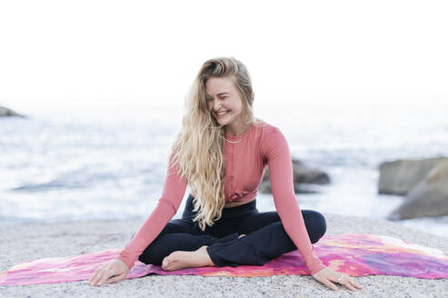 Glückliche junge Frau sitzt auf einer Übungsmatte vor dem Meer - MEF00161