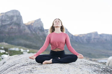 Young woman meditating on rock at beach - MEF00165