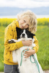 Happy boy stroking and embracing Border Collie dog on field - NJAF00201