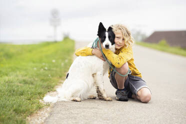 Smiling boy stroking Border Collie dog and crouching on road - NJAF00203