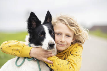 Lächelnder blonder Junge, der einen Border Collie Hund umarmt - NJAF00204