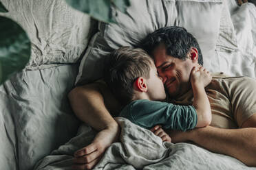 Lächelnder Mann mit schlafendem Jungen im Bett - VSNF00374