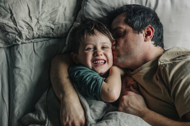 Man kissing son lying on bed in bedroom - VSNF00377