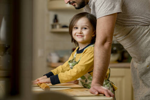 Lächelnder Sohn rollt Teig mit seinem Vater in der Küche zu Hause - ANAF00886
