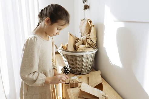 Cute girl opening gifts from advent calendar on cabinet at home - SSYF00043