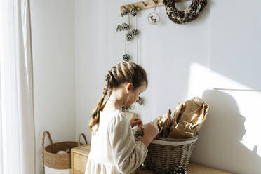 Girl with braided hair searching gifts in advent calendar basket - SSYF00052