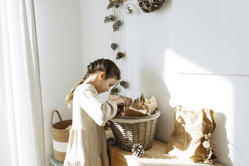 Girl with braided hair searching gifts in advent calendar basket at home - SSYF00053