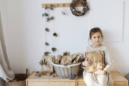 Smiling girl holding gift box from homemade advent calendar at home - SSYF00057