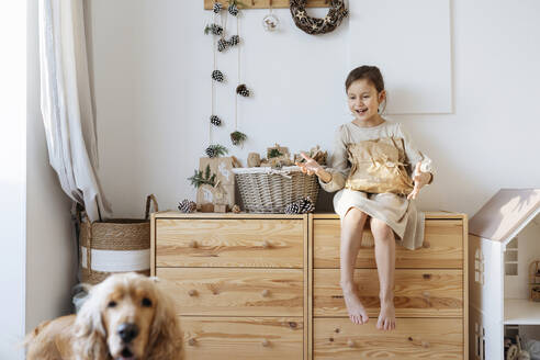 Happy girl looking at dog and gesturing in front of wall - SSYF00059