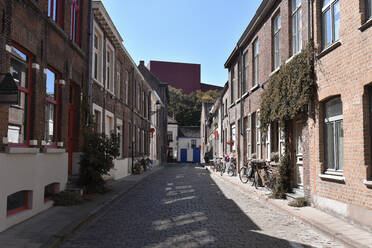 Belgien, Westflandern, Brügge, Leere Kopfsteinpflasterstraße mit Reihen von Stadthäusern auf beiden Seiten - FDF00352