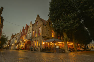 Belgien, Westflandern, Brügge, Kopfsteinpflaster vor einem Straßencafé und einer Reihe von Stadthäusern in der Abenddämmerung - FDF00357