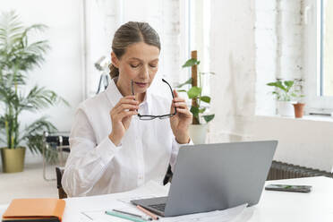 Mature businesswoman wearing eyeglasses sitting at office - VPIF07797